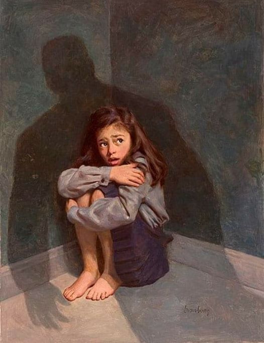 Young girl fearfully crouching on floor in a corner against a dark plain wall with shadow of a figure looming over her.  